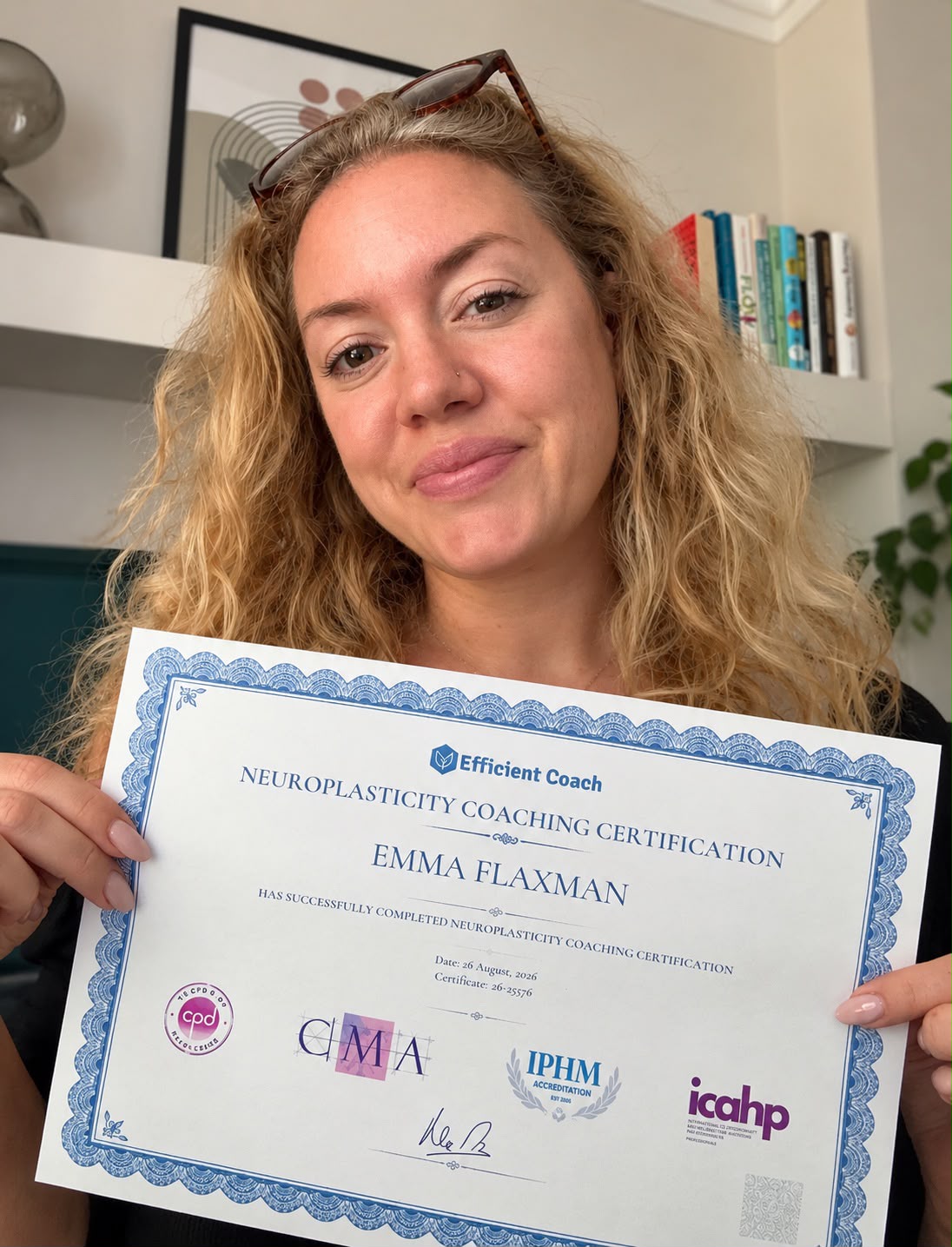 Emma Flaxman holding her neuroplasticity coaching certificate in front of bookshelves