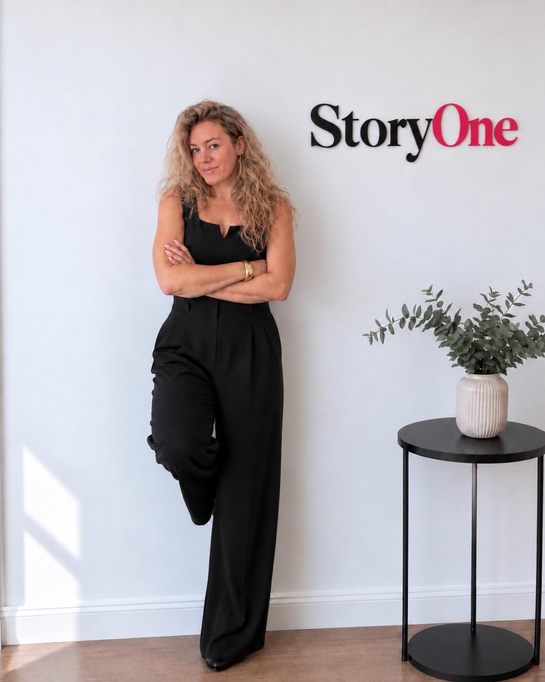 Emma Flaxman standing against a white wall beside the StoryOne sign