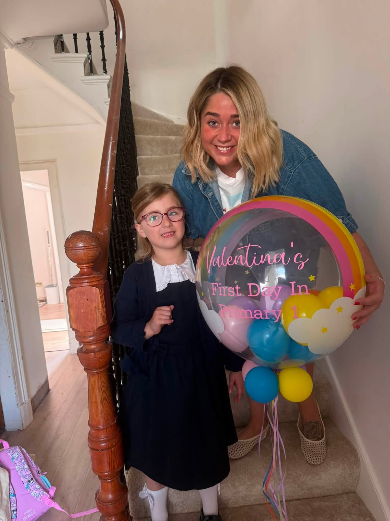 Adam Dowd's younger daughter on the stairs in her school uniform on her first day of primary school, beside a woman holding her balloon