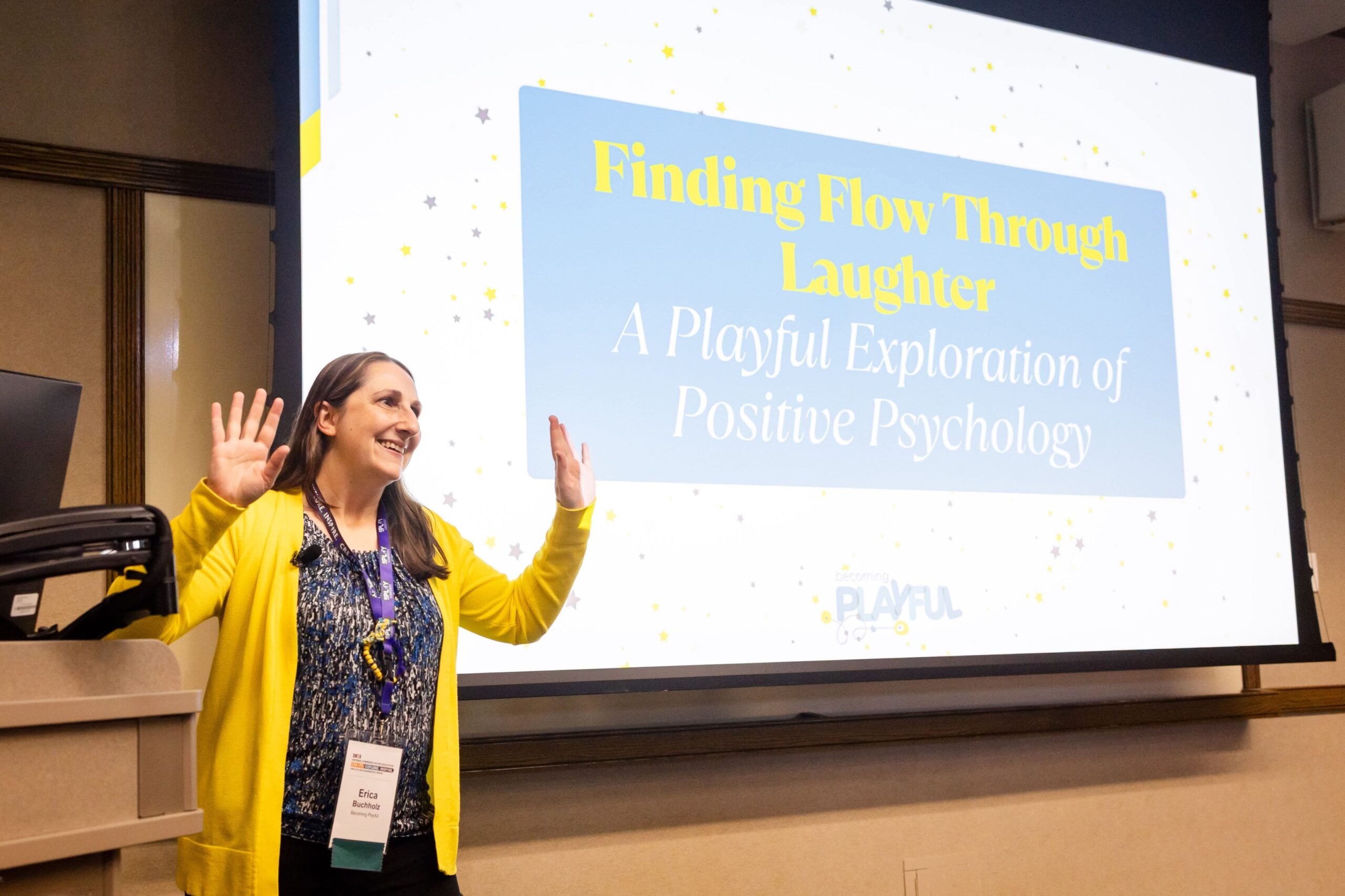 Erica Buchholz speaking in a yellow cardigan in front of a slide titled Finding Flow Through Laughter at a play conference