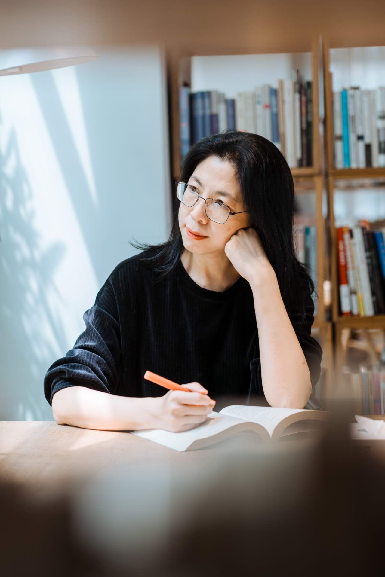 Xia Wu writing at a desk in front of a bookshelf
