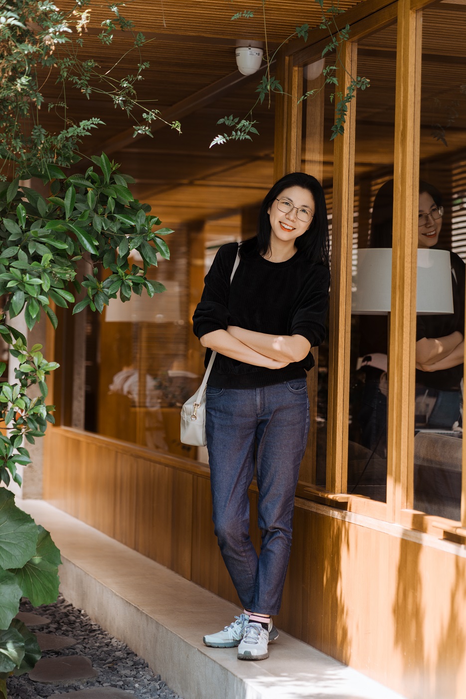 Xia Wu standing outside a wood-clad building, arms crossed, smiling