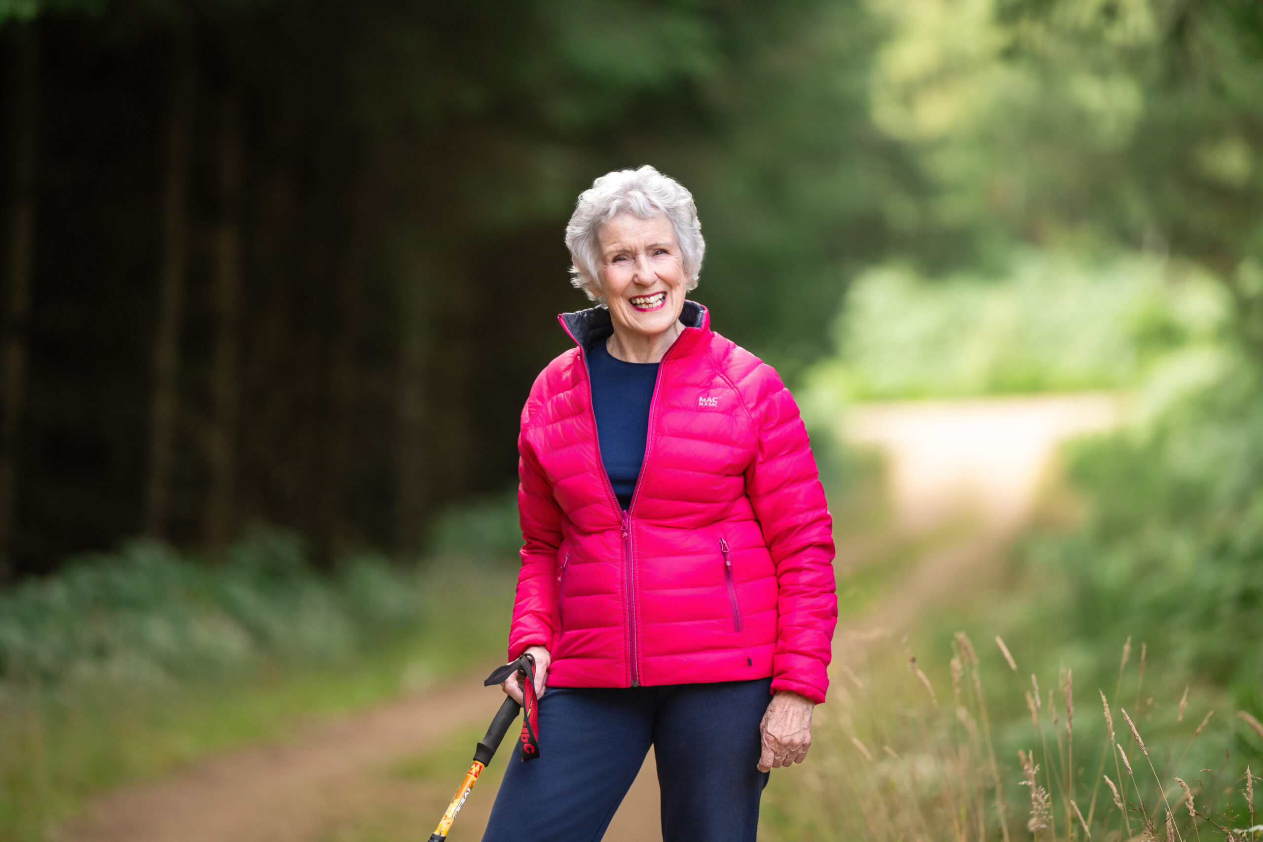 Rosee Elliott in a pink jacket with a walking pole on a forest track