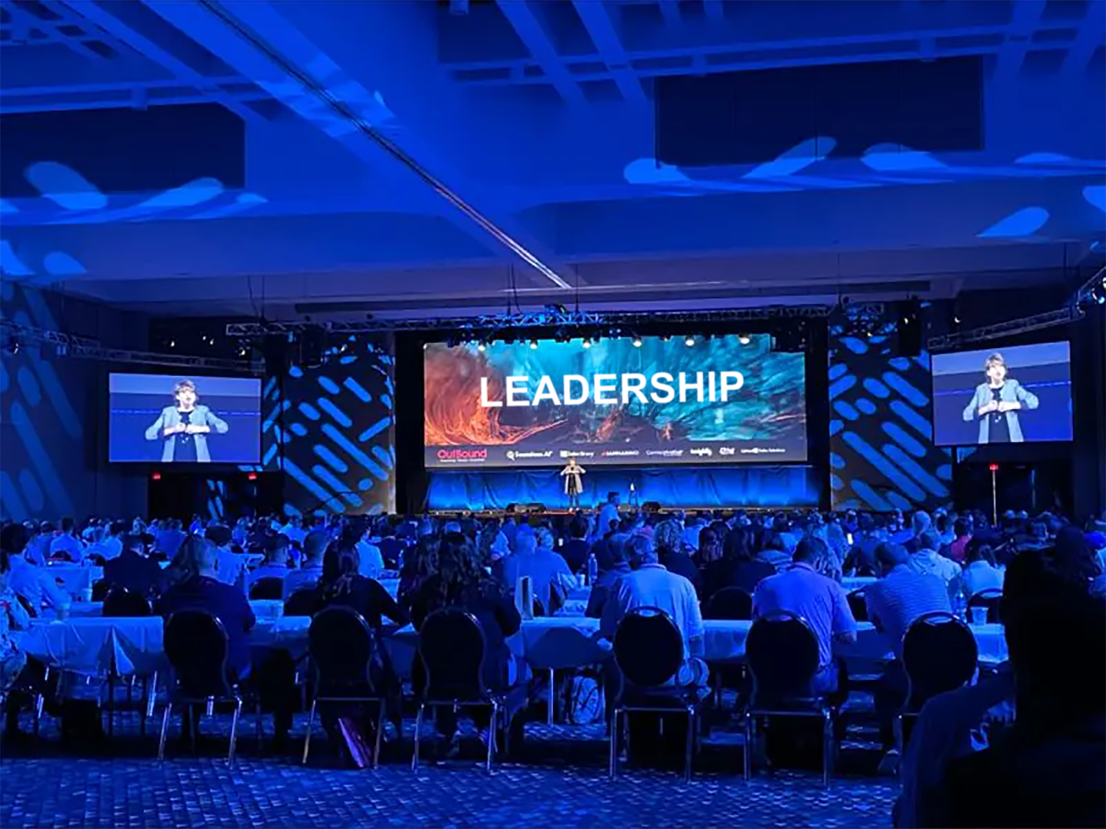 Bernadette McClelland on stage at the OutBound sales conference, the word Leadership on the screen behind her