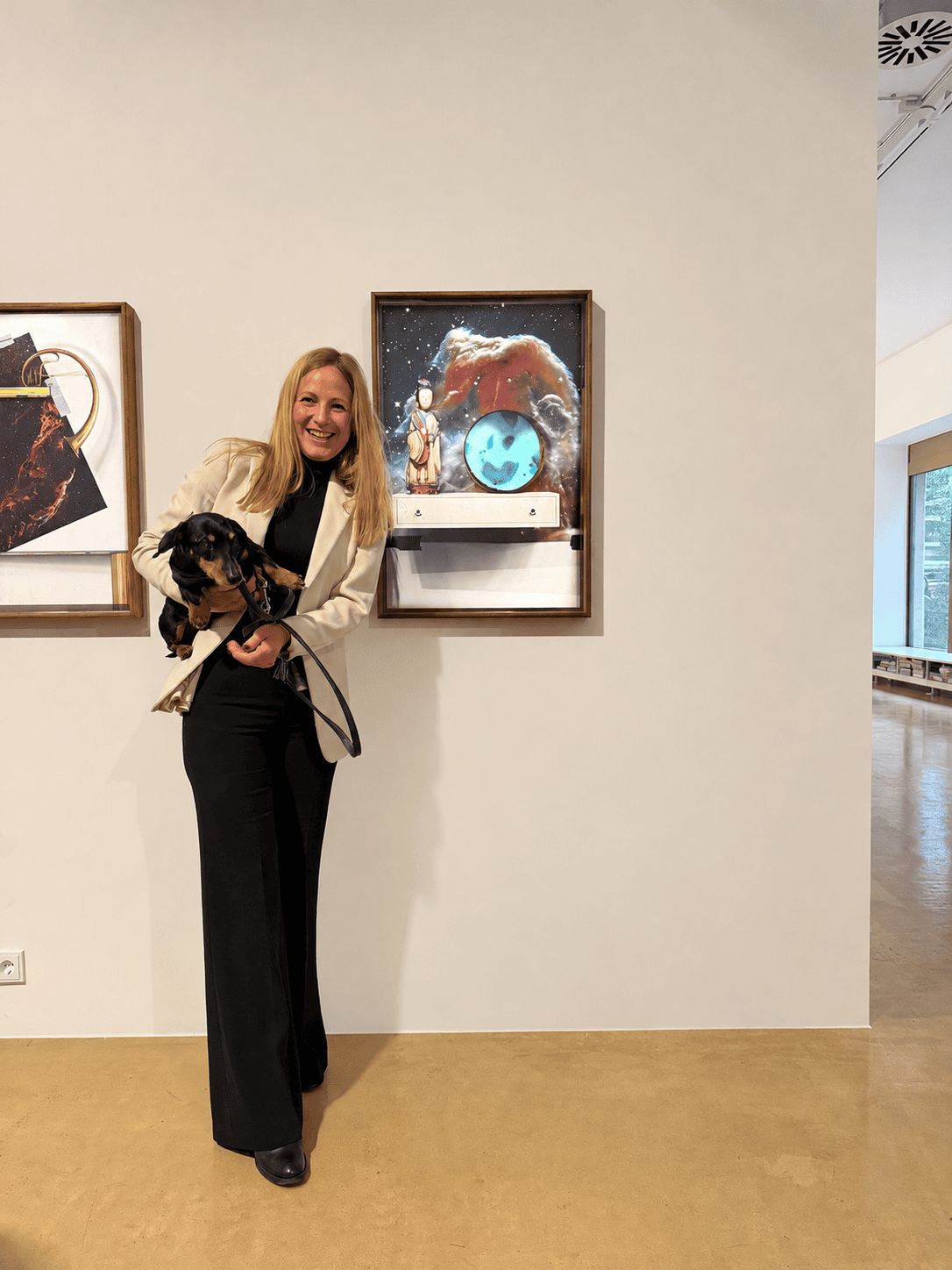 Dr. Annette Doms holding a dachshund on a lead in an art gallery beside a framed space artwork