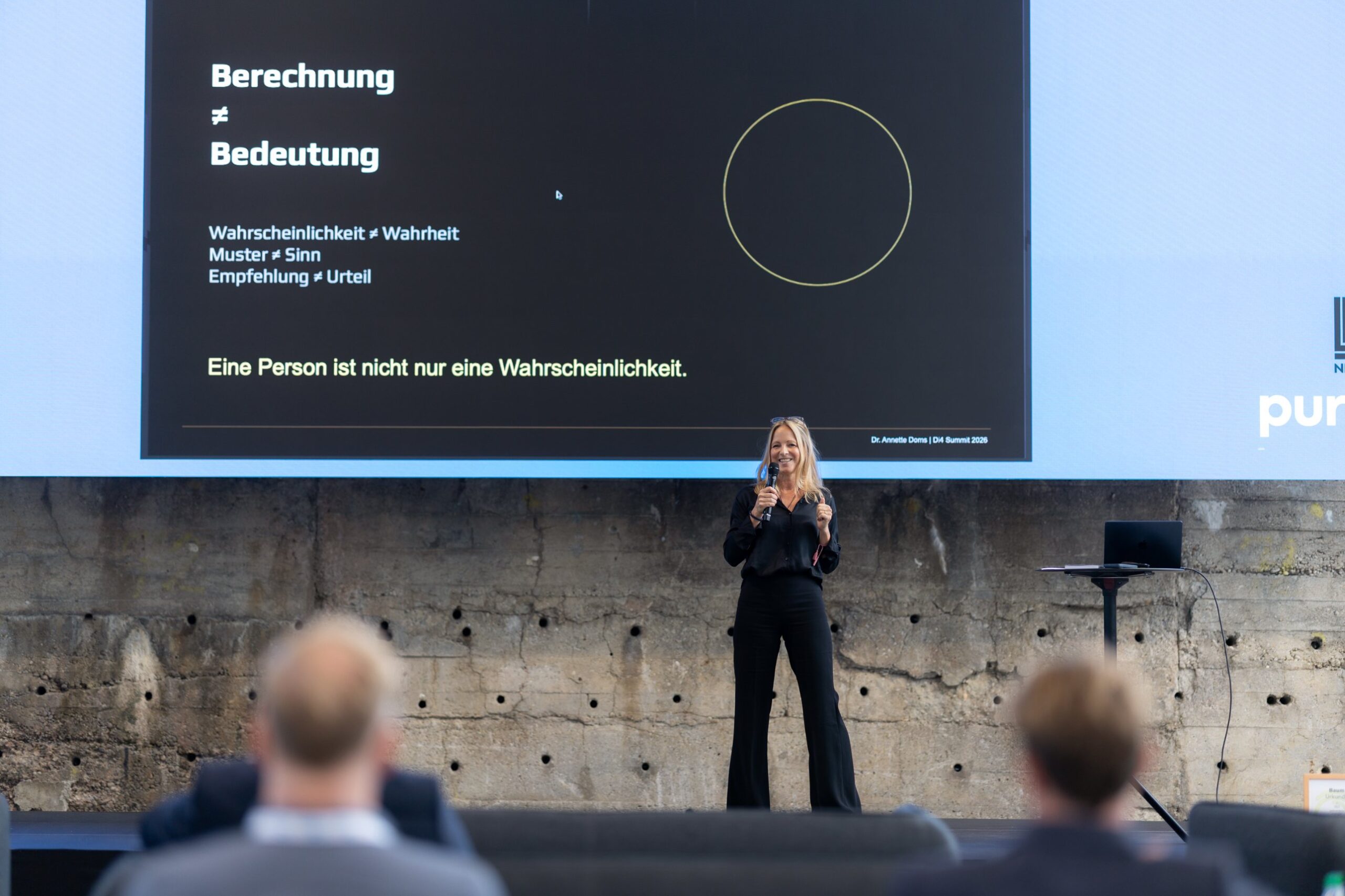 Dr. Annette Doms speaking with a microphone on stage at the Di4 Summit 2026, a slide behind her reading Berechnung ≠ Bedeutung