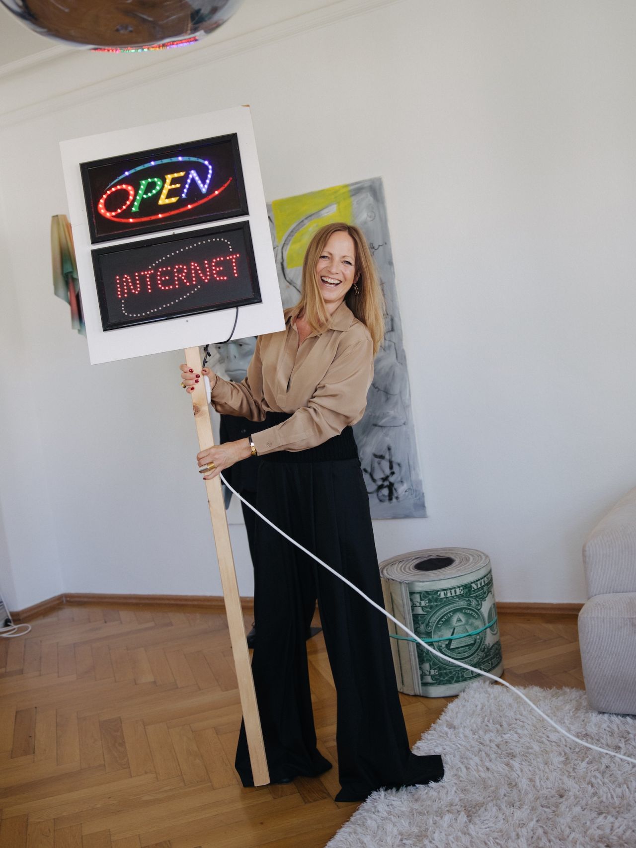 Dr. Annette Doms laughing as she holds a lit OPEN INTERNET sign in a bright room with art
