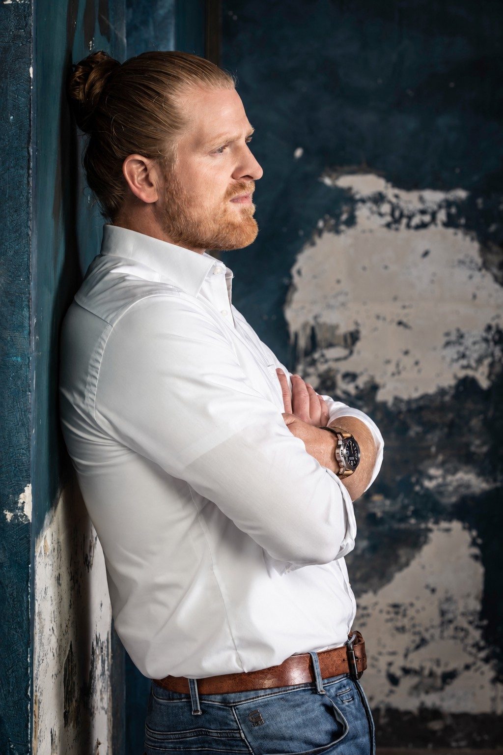 Frederic Lanz in profile, arms crossed, against a weathered blue wall