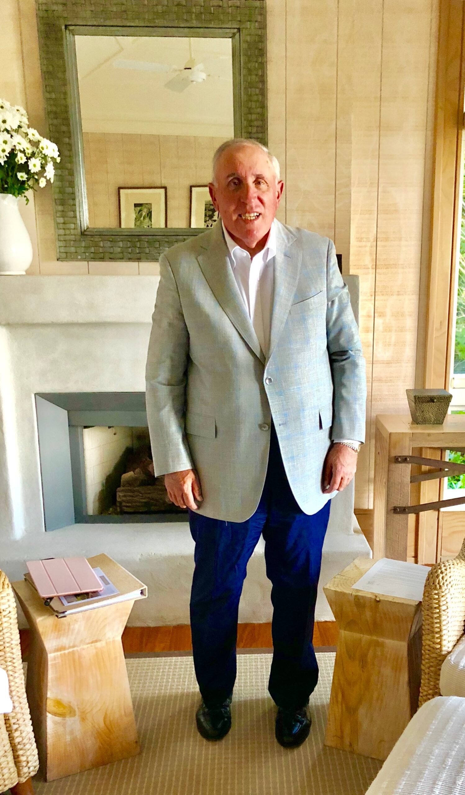Joseph R. Bronson in a grey blazer and navy trousers standing beside a fireplace