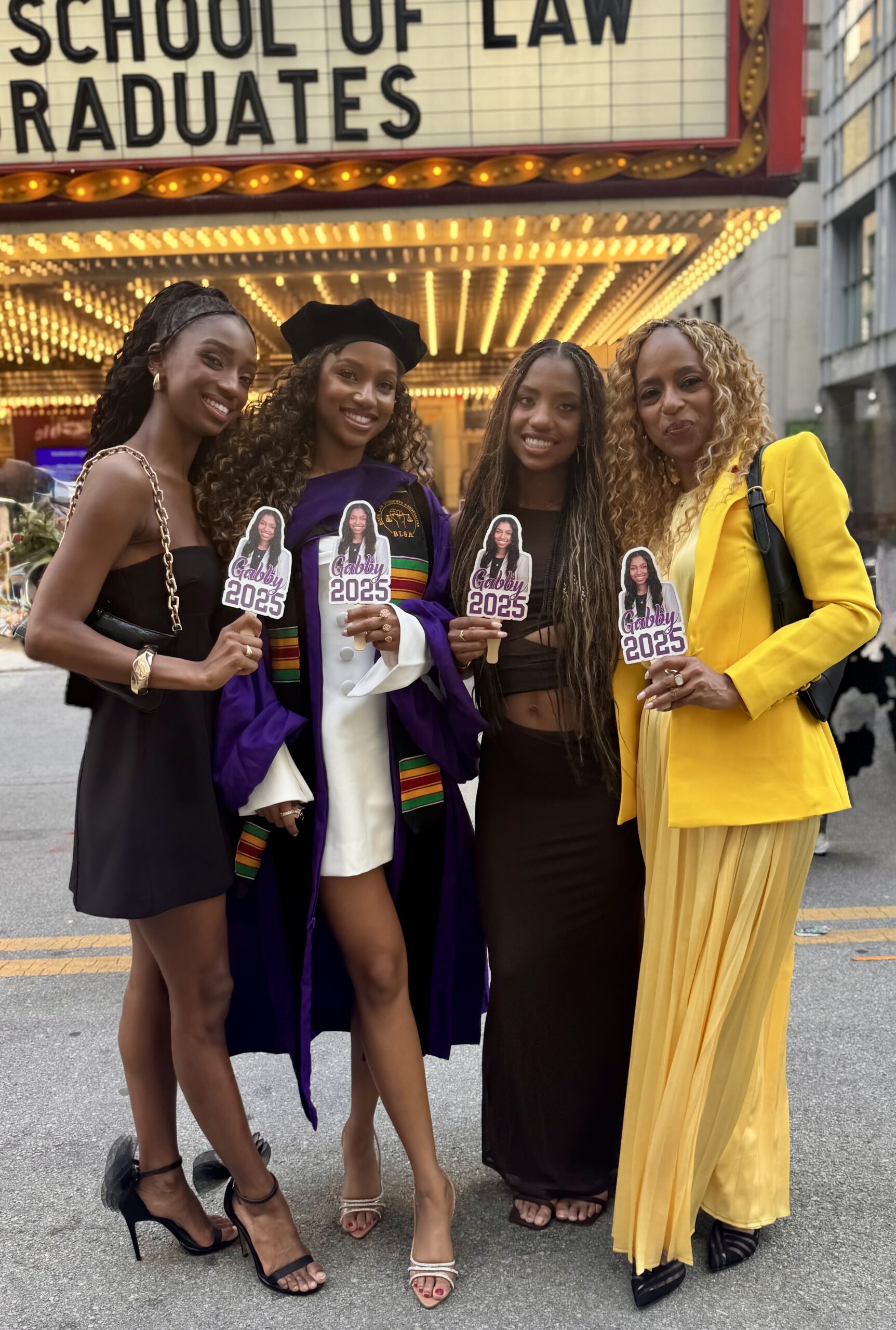 Michelle Patterson Wimes with her daughters outside a law school graduation, holding Gabby 2025 fans