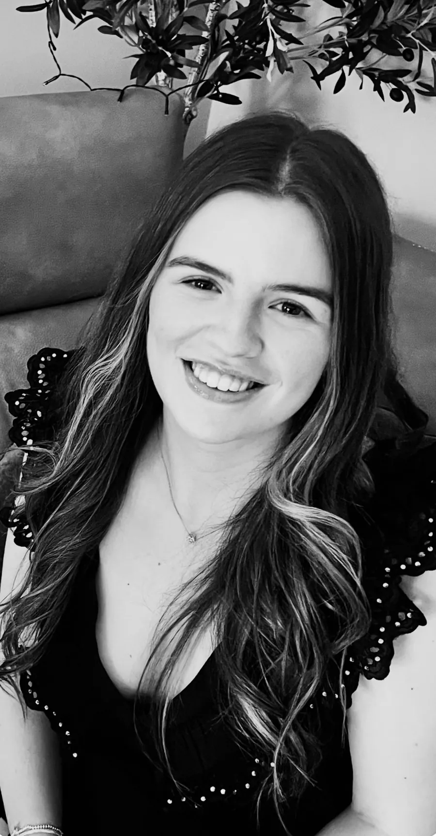 Black and white portrait of Poppy, daughter of Victoria Eagle, smiling and seated indoors