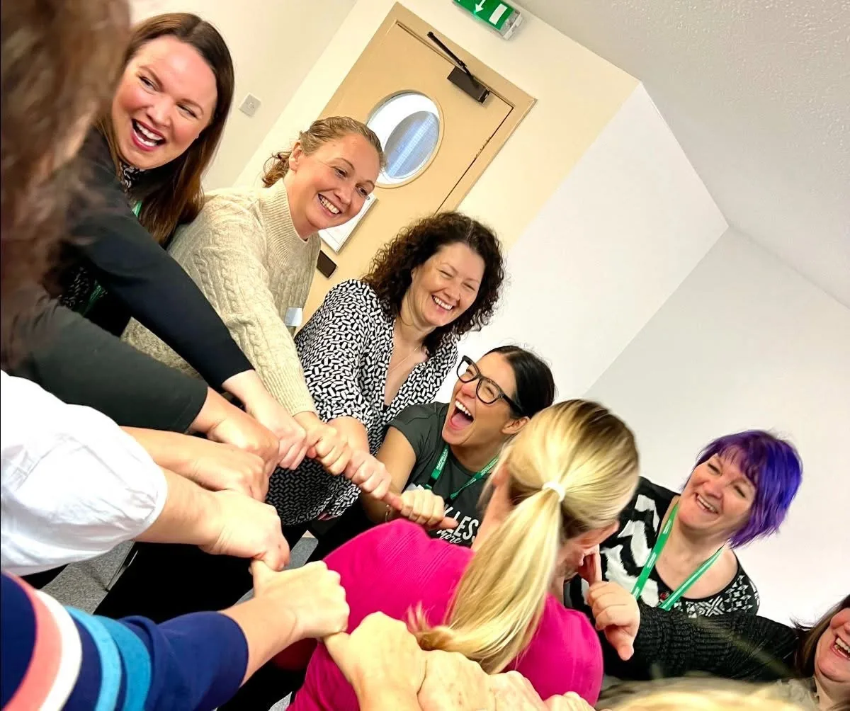 A Joyworks workshop group laughing with hands linked in a circle