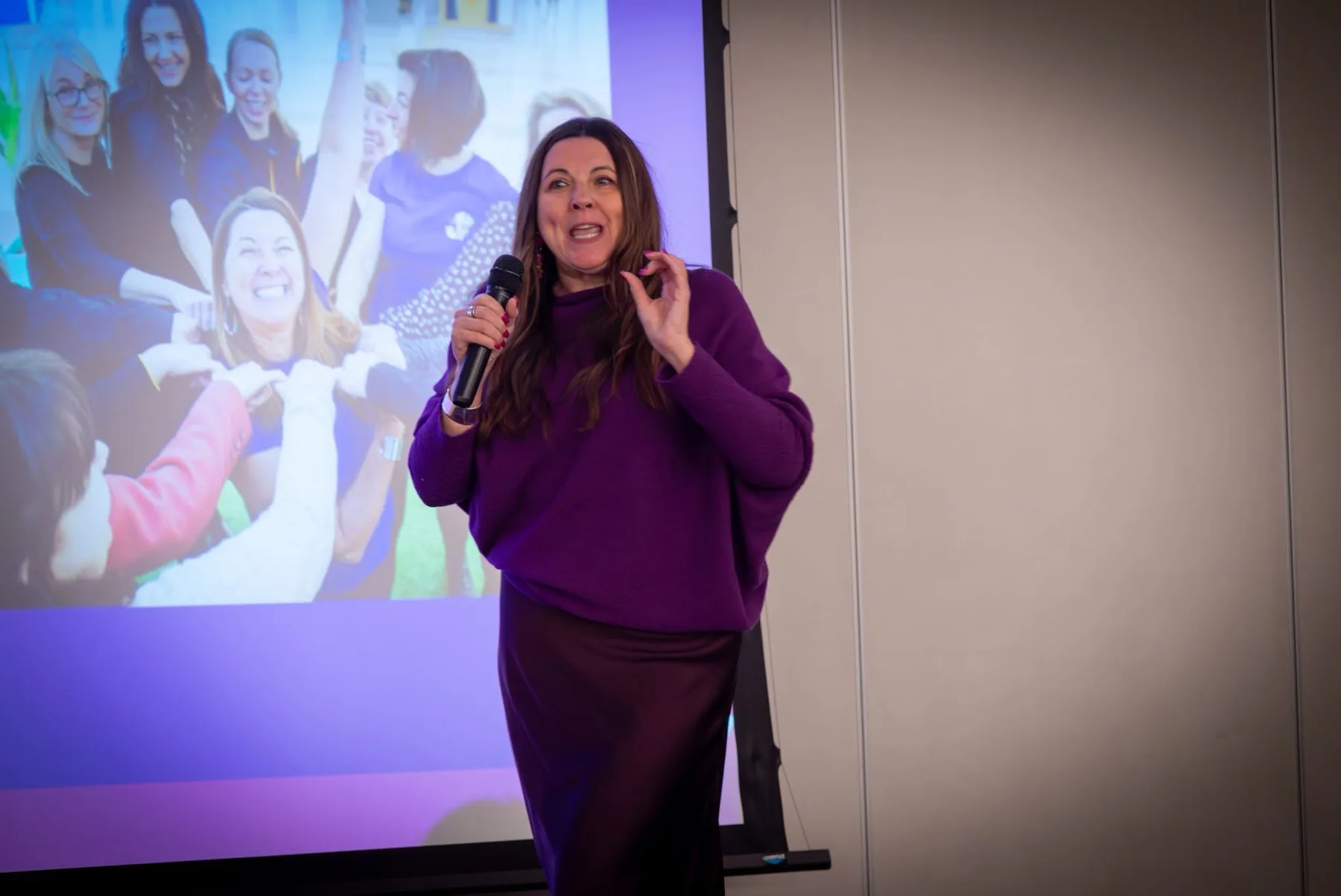 Sharon Miller speaking into a microphone in front of a projected slide